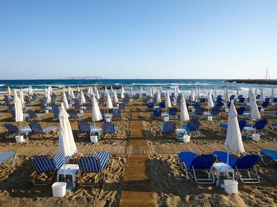 Spiaggia con file di lettini blu e ombrelloni bianchi sotto un cielo limpido