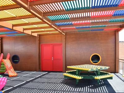 Area esterna coperta colorata con posti a sedere e scivolo vicino a un muro d'hotel.