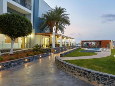 Sentiero lungo un hotel con palme e panchine illuminate al tramonto.