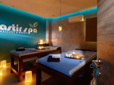 Accogliente sala massaggi con due lettini, luce di candele e atmosfera rilassante.