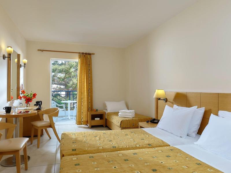 Camera d'hotel luminosa con due letti singoli, scrivania, sedie e vista sul balcone.