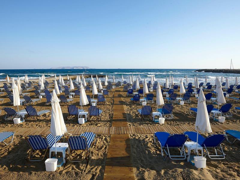 Spiaggia con file di lettini blu e ombrelloni bianchi sotto un cielo limpido