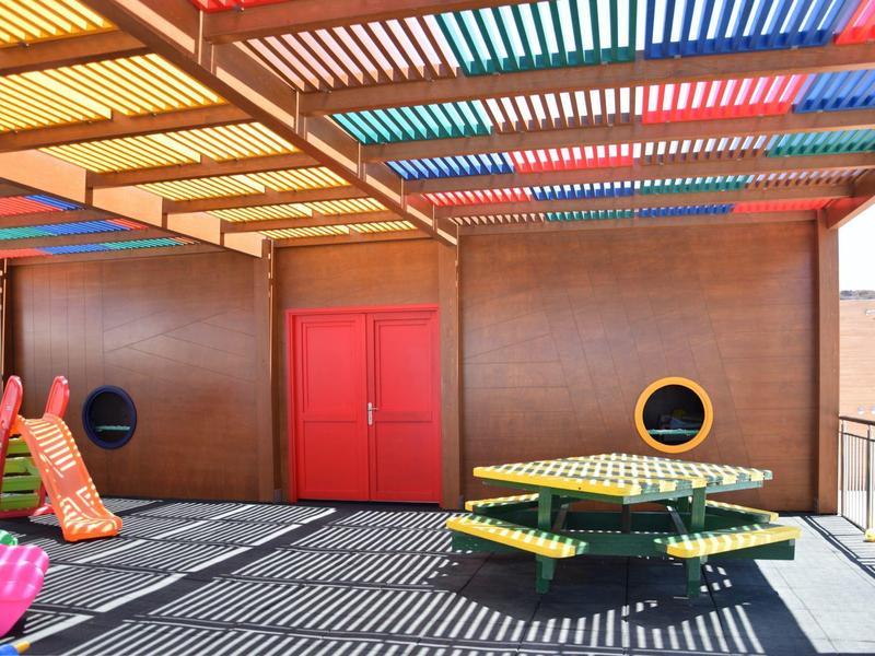 Area esterna coperta colorata con posti a sedere e scivolo vicino a un muro d'hotel.