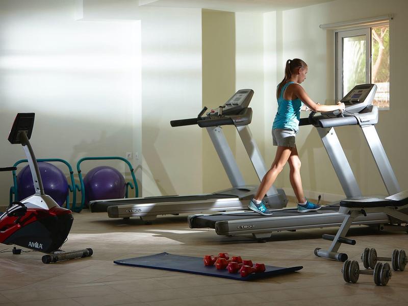 Donna che si allena su un tapis roulant in una palestra luminosa con varie attrezzature.