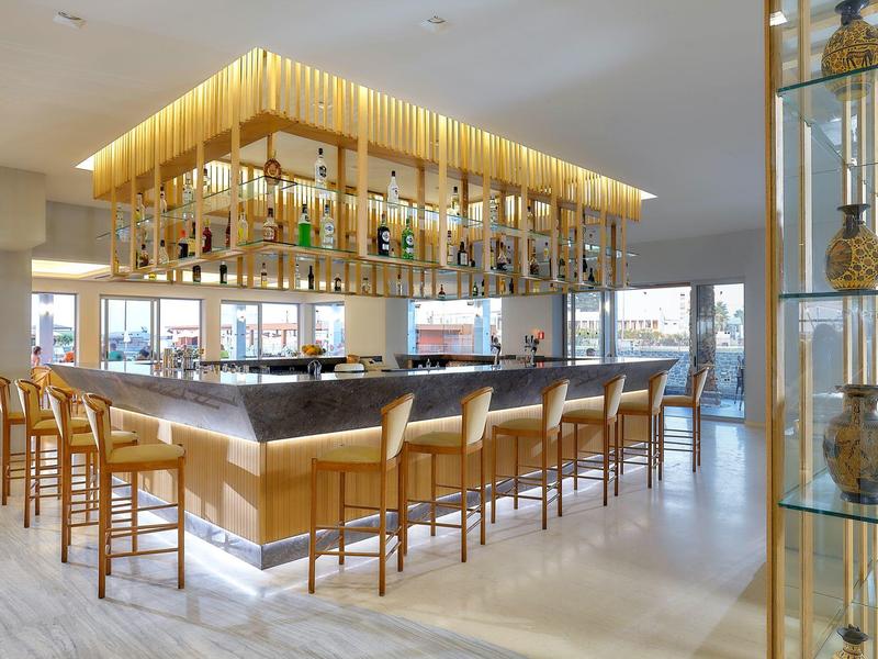 Bar dell'hotel moderna con sedie in legno, area bancone illuminata e grandi finestre.