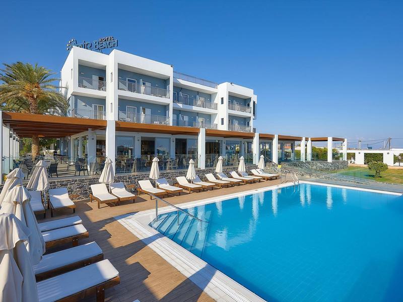 Hotel moderno con piscina all'aperto e lettini sotto un cielo azzurro.