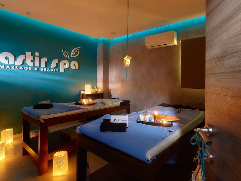 Accogliente sala massaggi con due lettini, luce di candele e atmosfera rilassante.