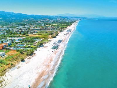 Langer Sandstrand mit klarem blauem Wasser und Gebäudeansammlungen entlang der Küste.