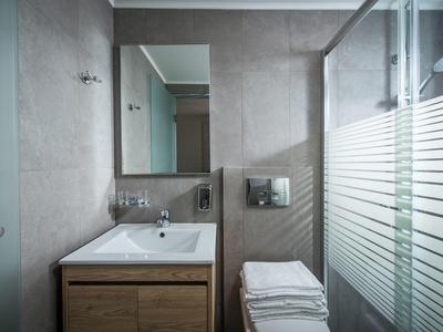 Baño moderno con lavabo, espejo grande y ducha de vidrio con patrón de rayas.