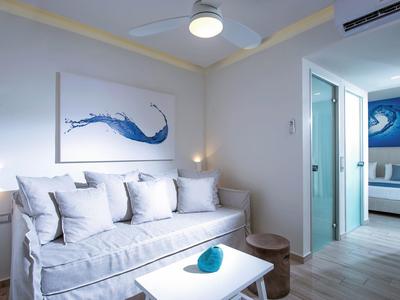 Habitación de hotel con decoración moderna, área de estar, arte azul y blanco y acceso a otra habitación.