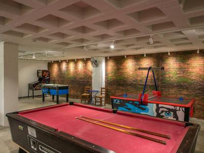 Spielzimmer mit Billardtisch, Airhockey und Tischfußball vor einer Backsteinwand.