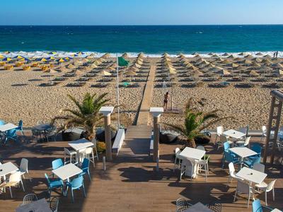 Playa con sombrillas y mesas cerca de un hotel junto al mar.