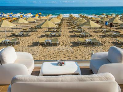 Moderne Sitzgruppe auf Terrasse mit Blick auf Strand mit Liegen und Sonnenschirmen am Meer.
