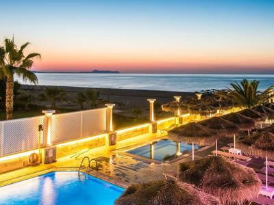 Beleuchteter Pool mit Palmen und Meerblick bei Sonnenuntergang.