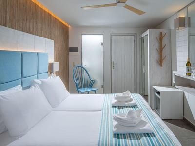Helles Hotelzimmer mit zwei Betten, blauen Akzenten und modernen Möbeln.