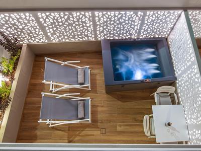 Moderner Balkon mit Holzfußboden, zwei Liegestühlen, TV und Tisch mit zwei Stühlen.
