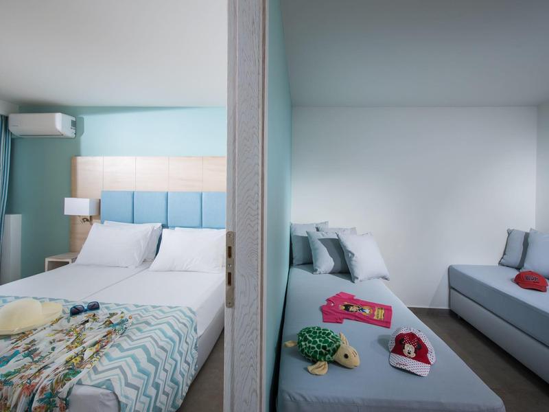 Dos habitaciones de hotel contiguas con camas, sofás y decoración sencilla.