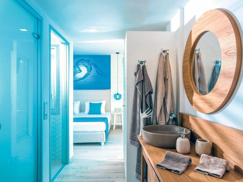 Habitación de hotel azul claro con baño moderno, cama doble y cuadro de ola en la pared.