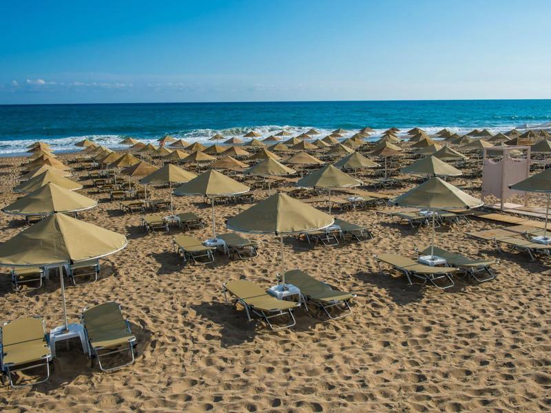 Una playa vacía con tumbonas y sombrillas organizadas bajo un cielo azul claro junto al mar.