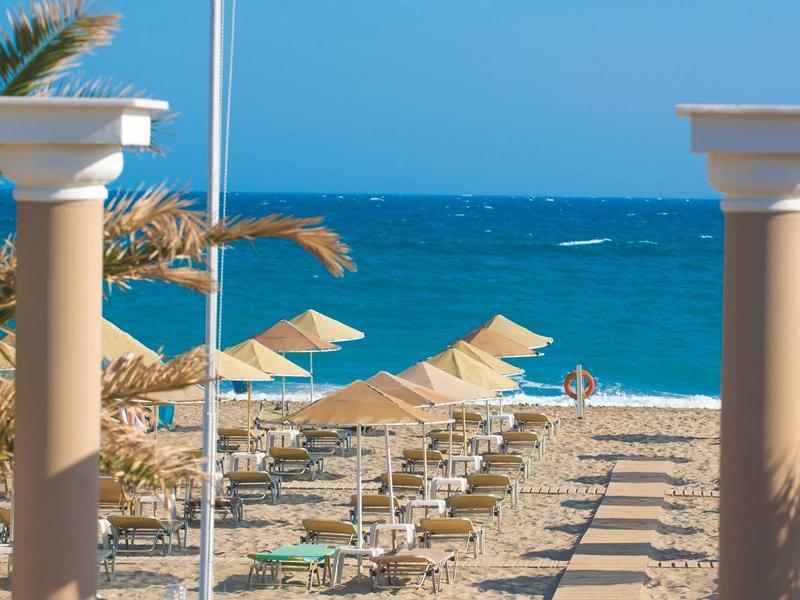 Playa con tumbonas y sombrillas, mar azul y cielo despejado bajo un sol radiante.