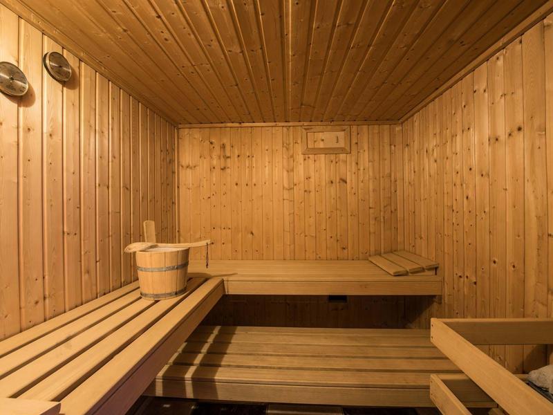 Sauna de madera con bancos de varios niveles y cubo para accesorios de sauna.