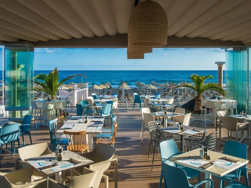 Restaurante abierto con vista al mar y varias mesas arregladas en una terraza.