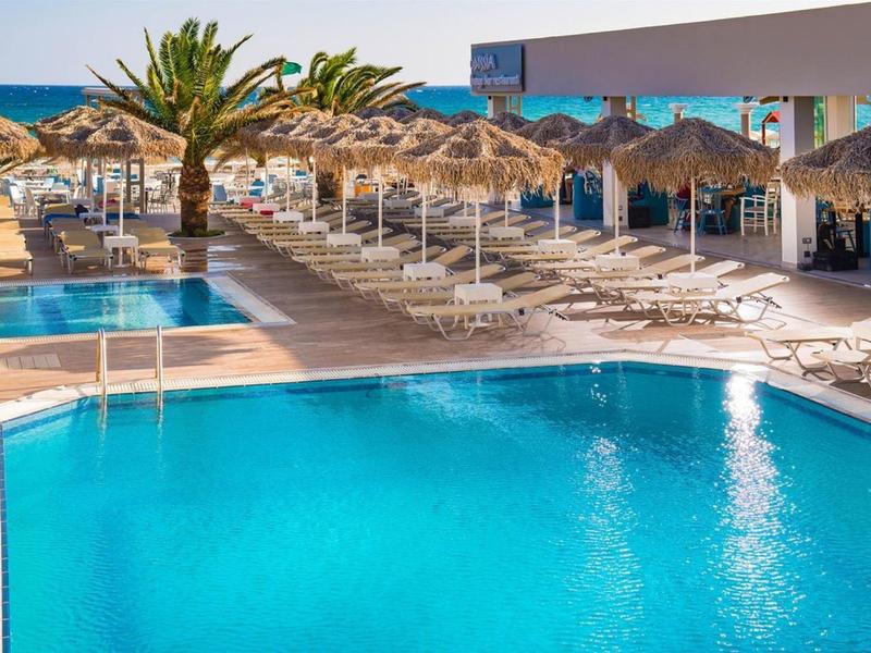 Gran piscina exterior con tumbonas y sombrillas de paja bajo un cielo soleado.