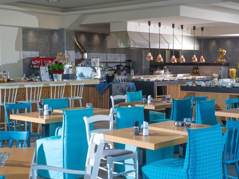 Comedor moderno de hotel con sillas azules y blancas y mesas de madera bajo lámparas blancas.