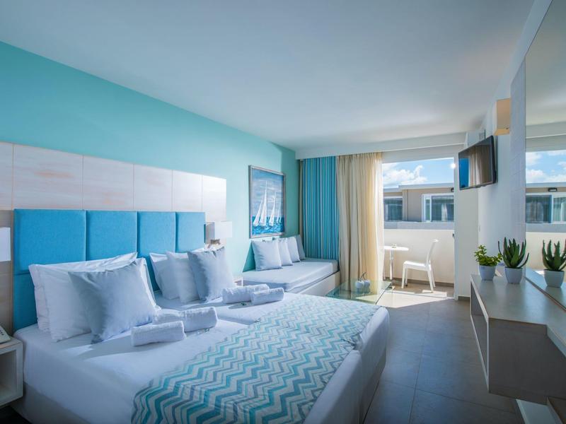 Habitación de hotel moderna con dos camas, detalles en azul y acceso a balcón con vistas al mar.