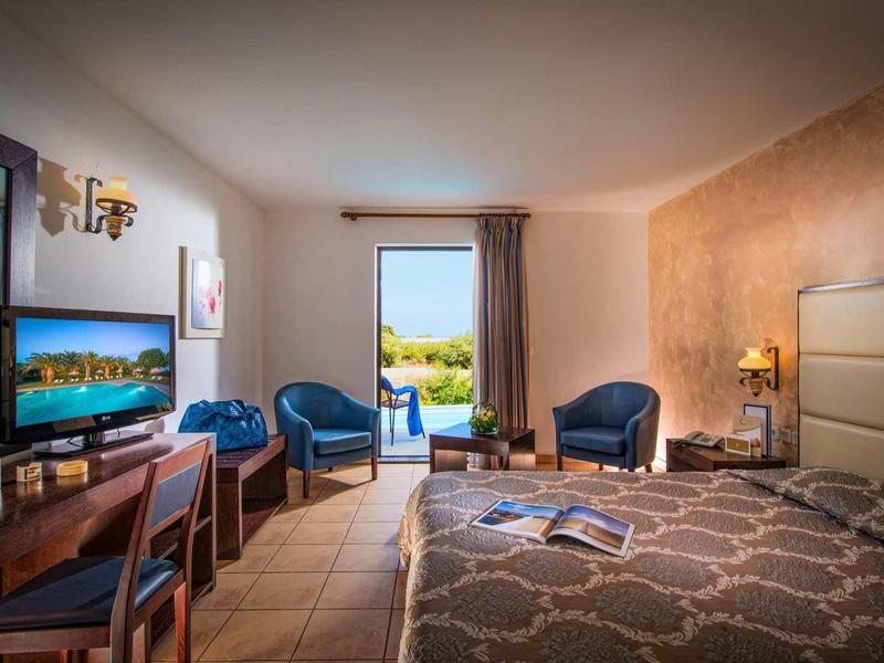 Accogliente camera d'hotel con letto matrimoniale, TV, zona salotto e balcone con vista.