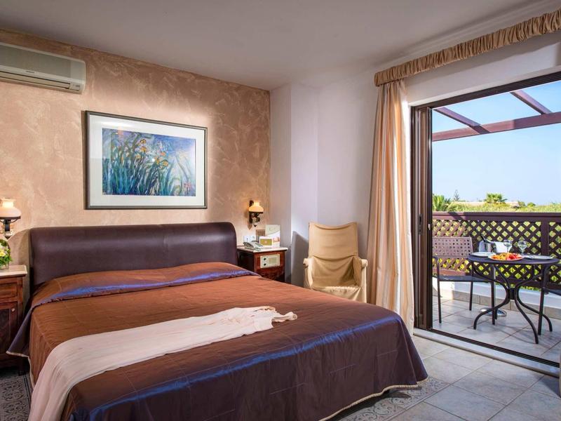 Camera d'hotel accogliente con letto matrimoniale, lampade da comodino e accesso a balcone con tavolo e sedie.