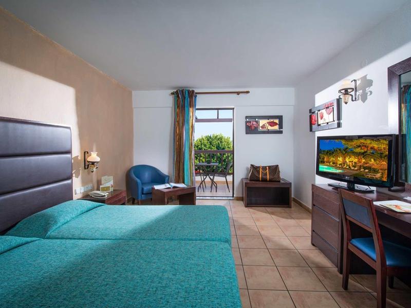 Camera d'hotel luminosa con letto matrimoniale, scrivania, TV e balcone con vista.