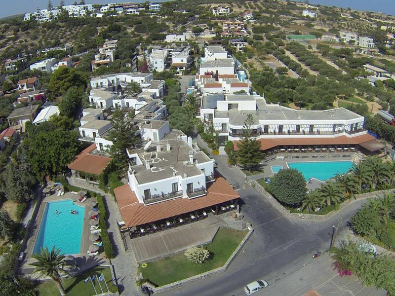 Veduta aerea di un hotel con due grandi piscine circondato da colline e edifici.