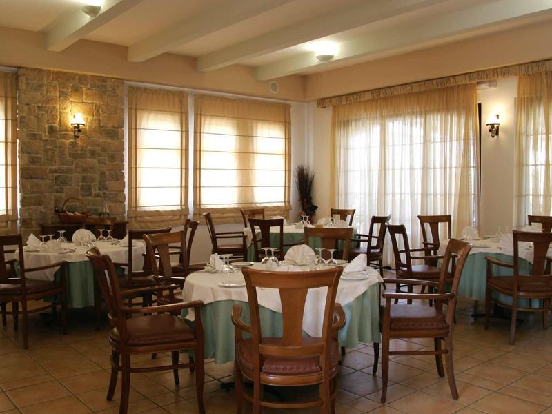 Ristorante con tavoli rotondi, pavimento in legno, grandi finestre, ambiente luminoso e accogliente.