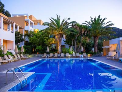 Piscine éclairée avec chaises longues et palmiers dans un hôtel au coucher du soleil.