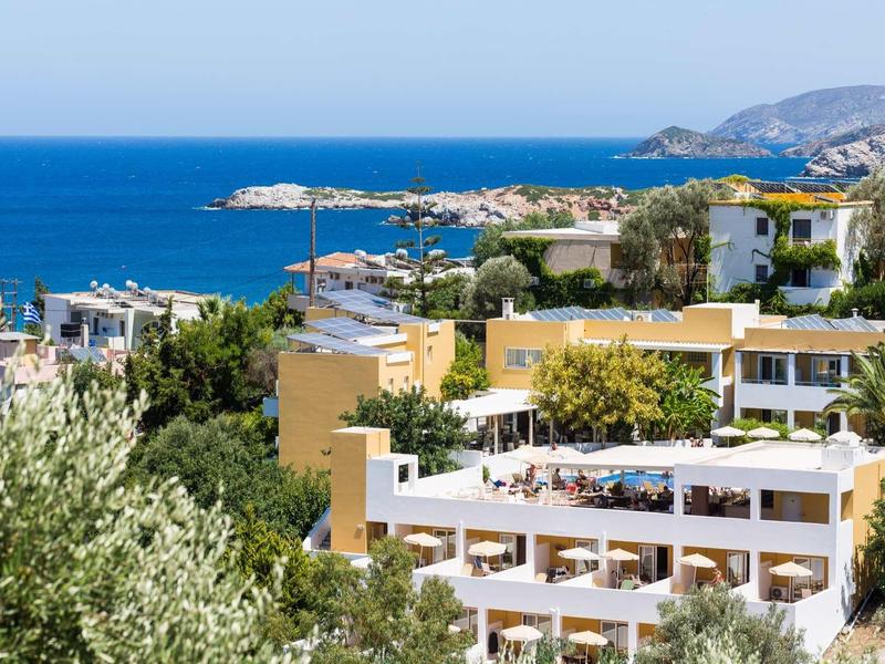 Complexe hôtelier avec terrasse près de la côte offrant une vue sur la mer bleue et les collines vertes.