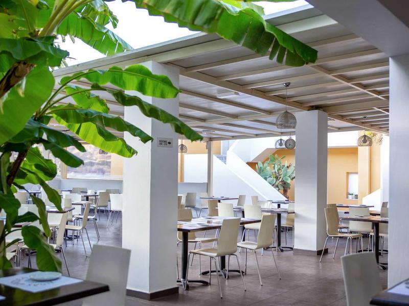 Salle à manger moderne avec mobilier blanc et plantes vertes dans un hôtel.