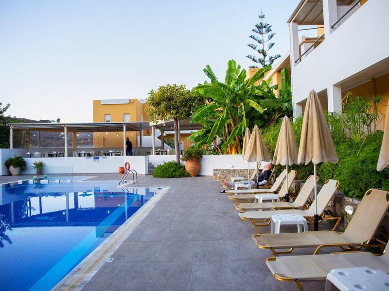 Espace piscine avec chaises longues et parasols à côté d'un bâtiment d'hôtel blanc.