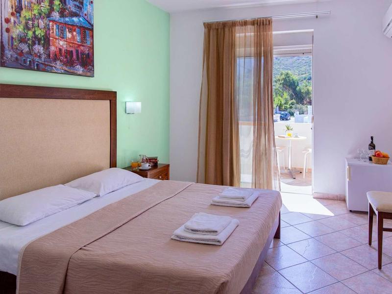 Chambre d'hôtel moderne avec lit double, balcon et murs verts et blancs lumineux.