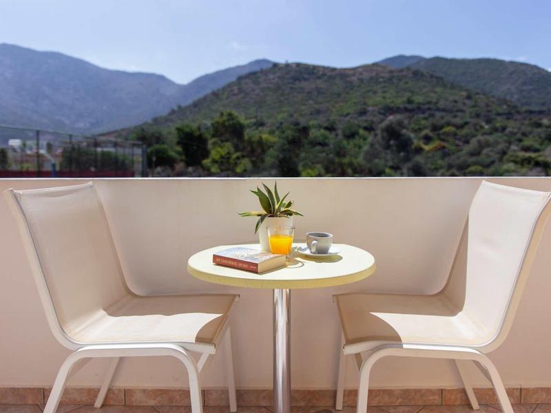 Deux chaises blanches avec une petite table sur une terrasse avec vue sur les montagnes.