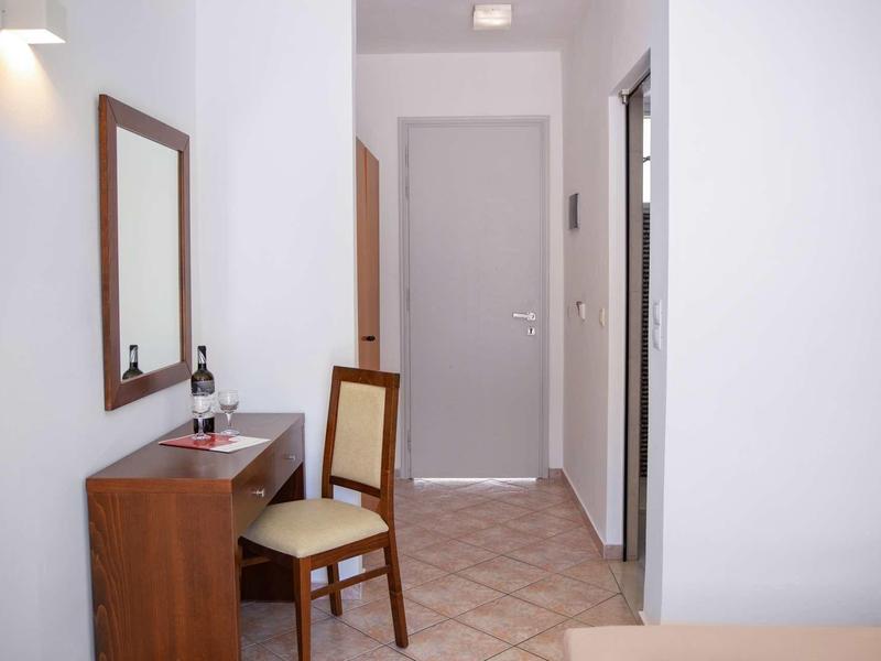 Petit couloir d'hôtel avec bureau, chaise, miroir et bouteille de vin.