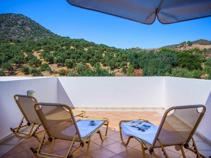 Balcon avec trois chaises et une table donnant sur des collines verdoyantes sous un ciel bleu.