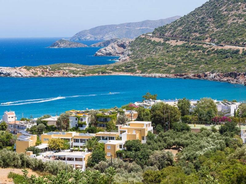 Vue sur une ville côtière avec des bâtiments méditerranéens, des collines et une mer bleue claire.