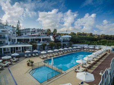 Modern hotel pool with many lounge chairs and umbrellas under a partly cloudy sky.