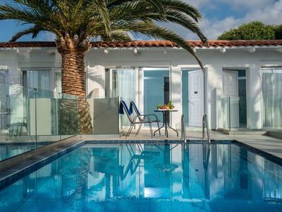 Modern pool with palm trees in front of white hotel rooms and patio furniture in clear weather.
