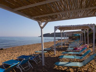 Beach with blue sun loungers and shade structures on sandy shore, calm sea in the background.