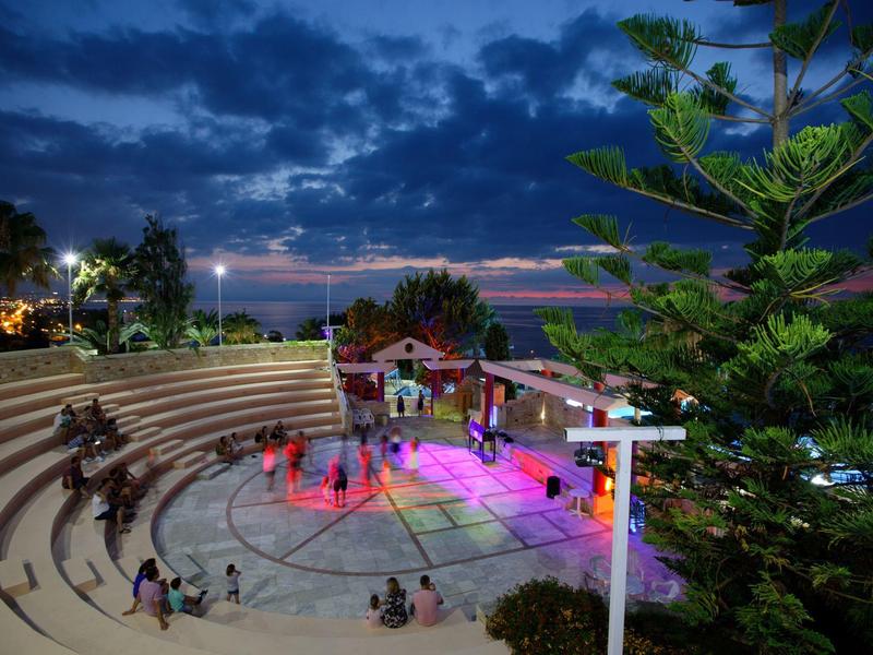 Evening outdoor stage with tiered seating and audience under cloudy dusk sky.