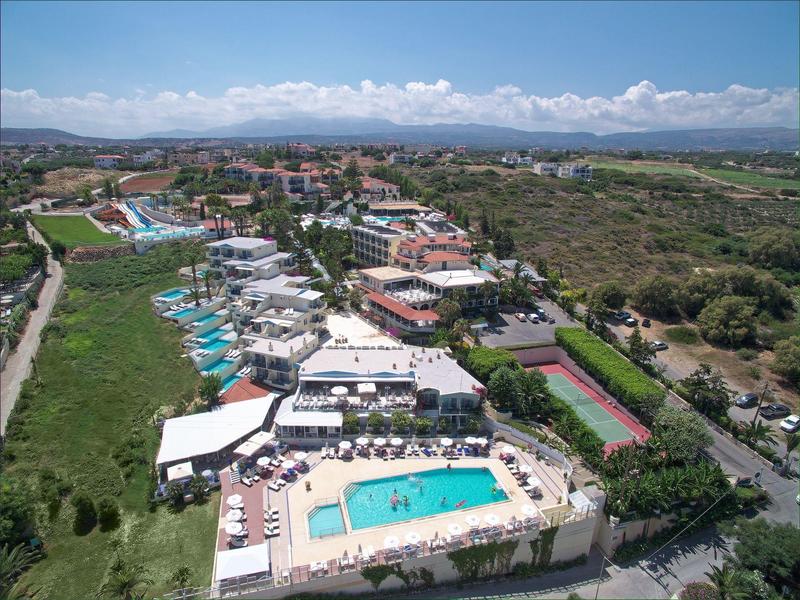 Aerial view of a hotel complex with swimming pool, sun umbrellas, and tennis court in a rural setting.