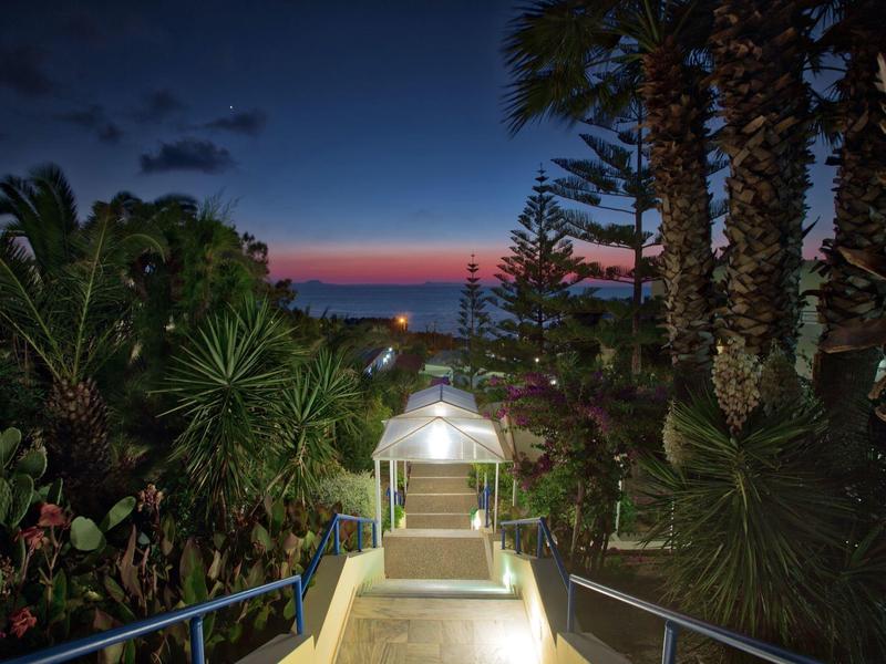 Illuminated path with tropical plants at sunset, sea view in the background.