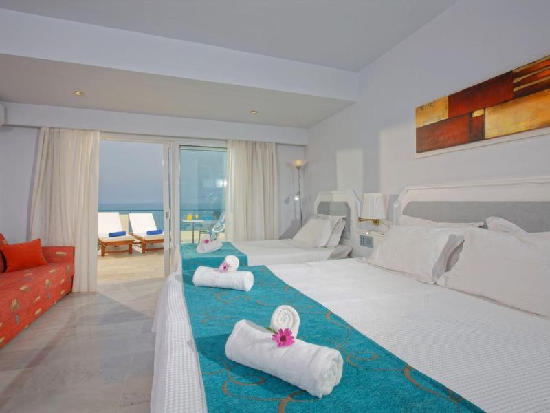 Modern hotel room with double bed, blue accents, and terrace with sea view.